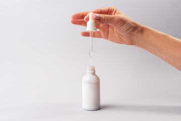 Hand of woman with pipette with drop of serum or hyaluronic acid or collagen moisturizer and white...