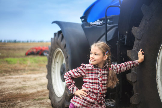 Cute girl near the modern tractor in the field.