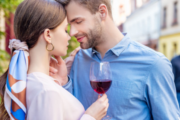 handsome boyfriend touching face of beautiful girlfriend holding glass of red wine