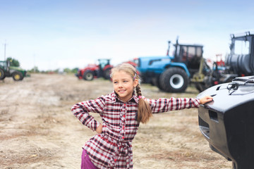 Cute girl near the modern tractor in the field.