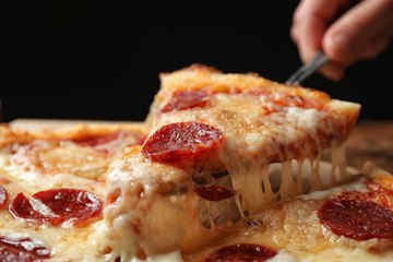 Woman taking slice of tasty pepperoni pizza at table, closeup