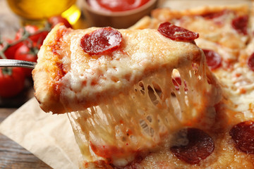 Taking slice of tasty pepperoni pizza on wooden table, closeup
