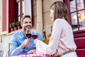 happy young couple clinking wine glasses while sitting at table in street cafe