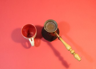 Copper cezva with cooked coffee and empty cup on red background