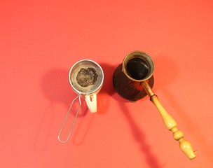 Copper cezva with cooked coffee and  cup with strainer on red background