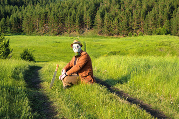 road field on it sits a man in a hat and gas mask next stuck in the ground sword