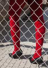 Woman's legs in red tights behind the metal mesh fence