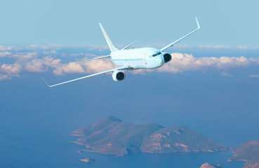 Fototapeta na wymiar Airplane fly above beautiful island - White passenger airplane in the clouds - Travel by air transport