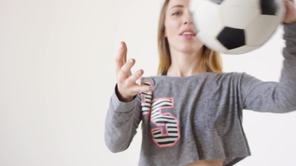 Mid-section studio shot of young sexy woman in fishnet tights, shorts and cropped sweatshirt throwing soccer ball and then posing for camera against white background - Powered by Adobe