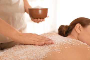 Young woman having body scrubbing procedure with sea salt in spa salon, closeup