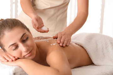 Young woman having body scrubbing procedure with sea salt in spa salon