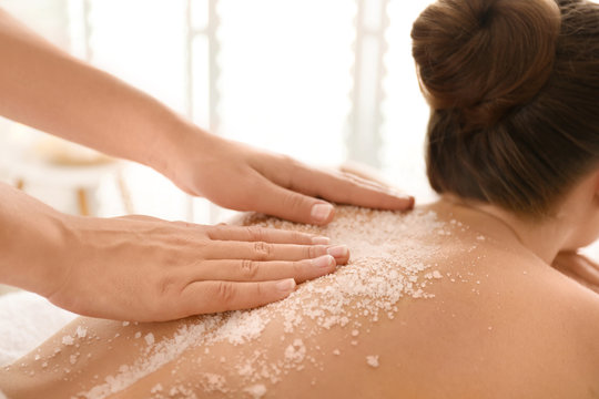 Young woman having body scrubbing procedure with sea salt in spa salon, closeup