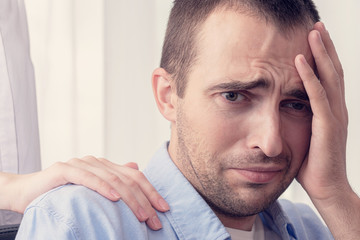 Obraz premium Concept of psychological assistance in the family. Portrait of a sad man, husband is depressed, wife puts her hand on man's shoulder, close up, toned