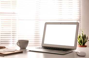 Fototapeta premium Laptop on desk near window in office. Comfortable workplace
