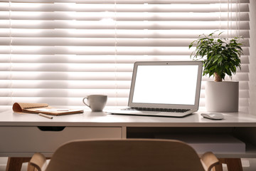 Laptop on desk near window in office. Comfortable workplace