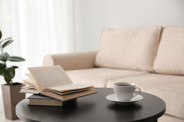 Books and cup of tea on table near modern sofa indoors. Home interior