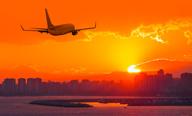 Commercial airplane flying above city in sunset 