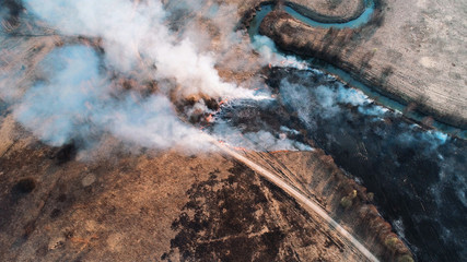 Strong fire in an empty field, heavy smoke from a burning place. The spread of the fire is stopped by a small river.