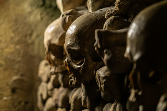 Skulls and bones in catacombs. Old broken skull placed in the wall of bones. Grim lighting. Underground cemetery
