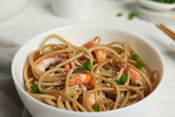 Tasty buckwheat noodles with shrimps in bowl on white wooden table, closeup
