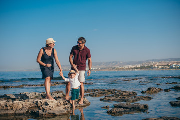 Family with a child stand on the stones against the background of the sea.