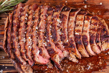 Close Up of Chopped Grilled Steak Rib Eye on Rustic Cutting Board on Wooden Background. Juicy Medium Ribeye Steak with Salt, Pepper and Rosemary. Concept of Delicious Meat Food. Top View