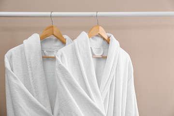 Fresh white bathrobes hanging on rack near beige wall
