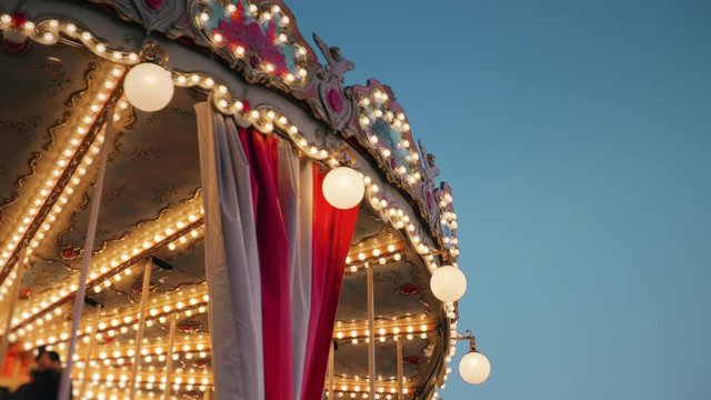 Beautiful view to the top of the spinning carousel with its festive decorations and glittering golden lights against dark evening sky.