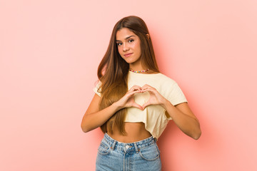 Young slim woman smiling and showing a heart shape with hands.