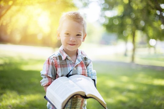 Closeup shot of a child holding an open bible while looking at the camera with blurred background