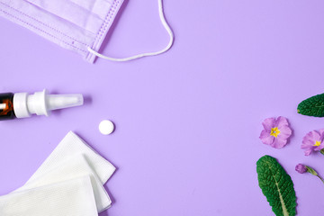 Allergy concept. Creative flat lay concept of seasonal spring and summer pollen allergy with napkins, pills, face mask, drops bottle and flowers on purple background. Top view, copy space