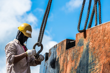 Technician rigger checking crane hook sling safety before lifting heavy steel product outside the...