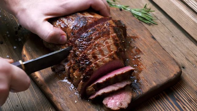 Chef with Vintage Knife Cuts of Grilled Beef Steak on Rustic Cutting Board on Wooden Background. Juicy Sliced Rib Eye Steak with Salt. Concept of Delicious Meat Food