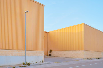 Nave industrial de con paredes amarillas en una calle vacía con un cielo azul