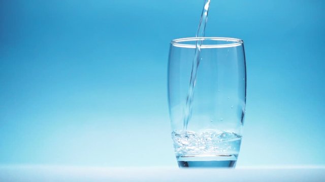 water is poured into a glass on blue background