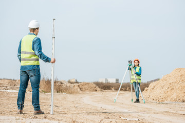 Surveyors using digital level and survey ruler on dirt road