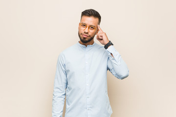 Young south-asian business man pointing temple with finger, thinking, focused on a task.