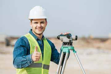 Smiling surveyor with digital level showing thumb up gesture