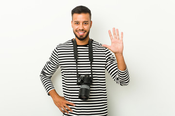 Fototapeta premium Young south-asian photographer smiling cheerful showing number five with fingers.