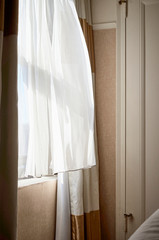 Fototapeta na wymiar Cortina movida por el viento en un día luminoso en una habitación en tonos ocres y blancos