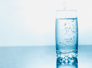 Drinking water poured into a glass isolated over blue abstract background
