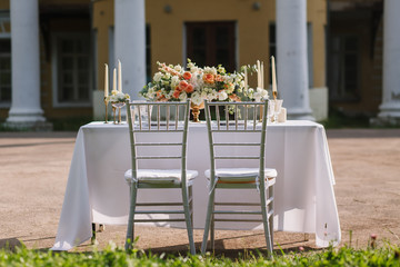 Wedding decoration table in the garden the style vintage on outdoor, floral arrangement. Decorated white table with flowers, served for two people, on the background of old building. Fine art laying.