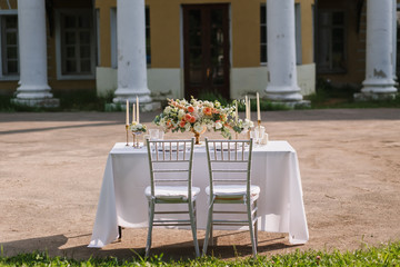 Wedding decoration table in the garden the style vintage on outdoor, floral arrangement. Decorated white table with flowers, served for two people, on the background of old building. Fine art laying.