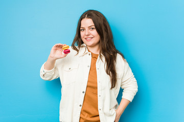 Young curvy woman holding macaroons happy, smiling and cheerful.