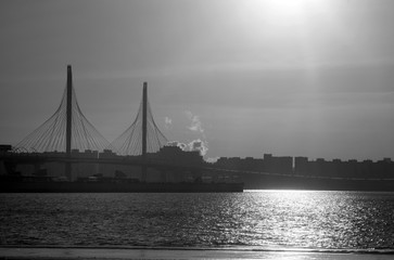 Modern bridge with buildings on the background of the water of the bay in St. Petersburg with glare of the sun on the water with backlight.
