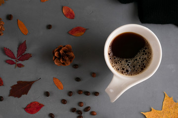 A mug of strong, hearty, brown, rich coffee on a gray concrete background with red and yellow leaves of mountain ash, oak, maple