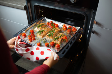 Cooking salmon in the oven. Housewife is preparing dinner. The chef is cooking red fish. Cooking fish in the oven. Girl takes out baked salmon with cherry rinds from the oven