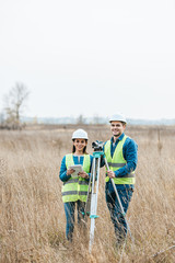 Surveyors with digital level and tablet smiling at camera in field