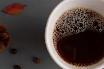A mug of strong, hearty, brown, rich coffee on a gray concrete background with red and yellow leaves of mountain ash, oak, maple