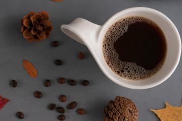 A mug of strong, hearty, brown, rich coffee on a gray concrete background with red and yellow leaves of mountain ash, oak, maple